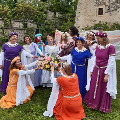 Il gruppo Danticadanza indossa abiti colorati medievali e si raduna attorno a un bouquet, nel giardino del Castello di Pergine.